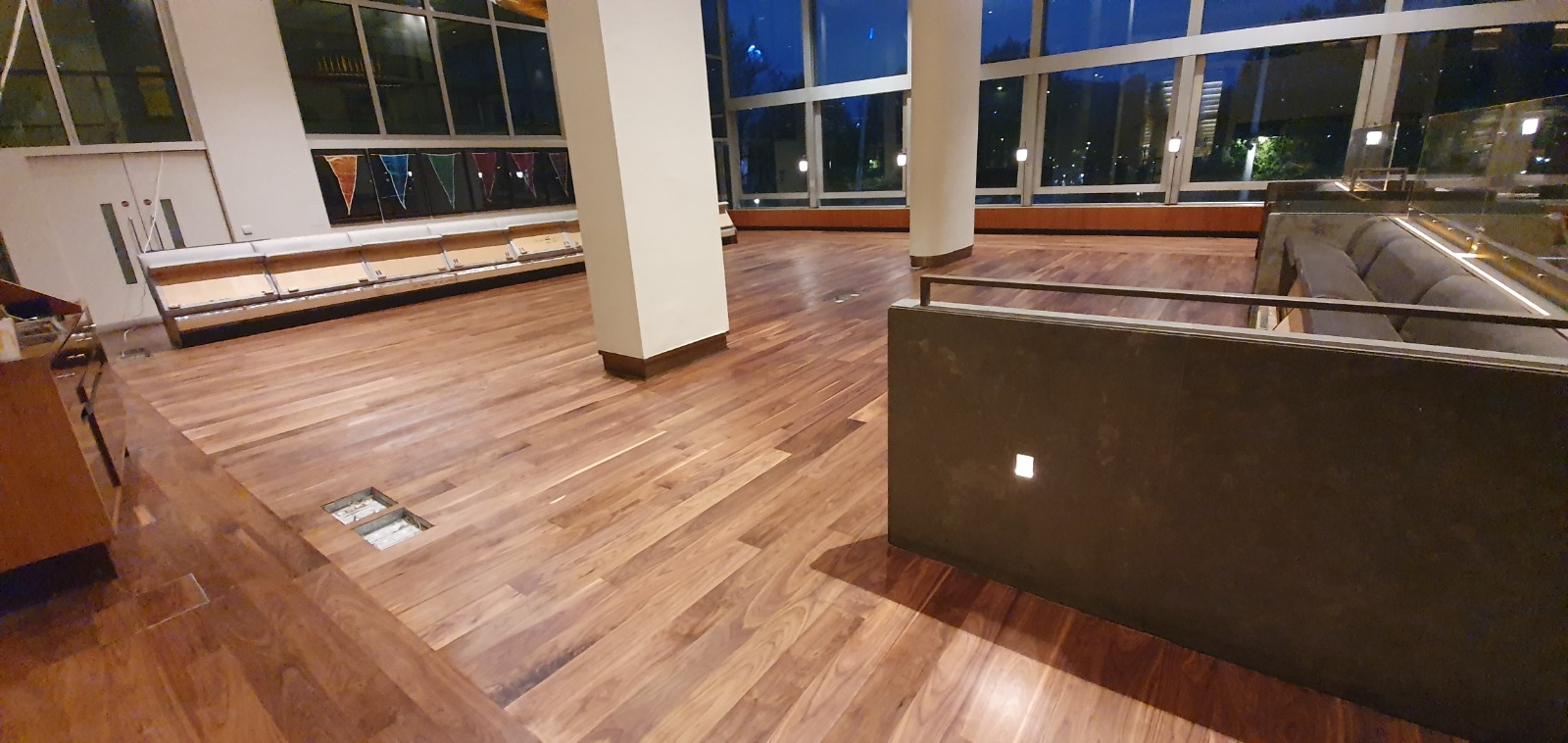 Restaurant Floor Sanding in Honoroak, showing a modern dining lounge at night with freshly sanded and sealed engineered hardwood plank flooring in a rich walnut tone, wide windows and built-in banquette seating.