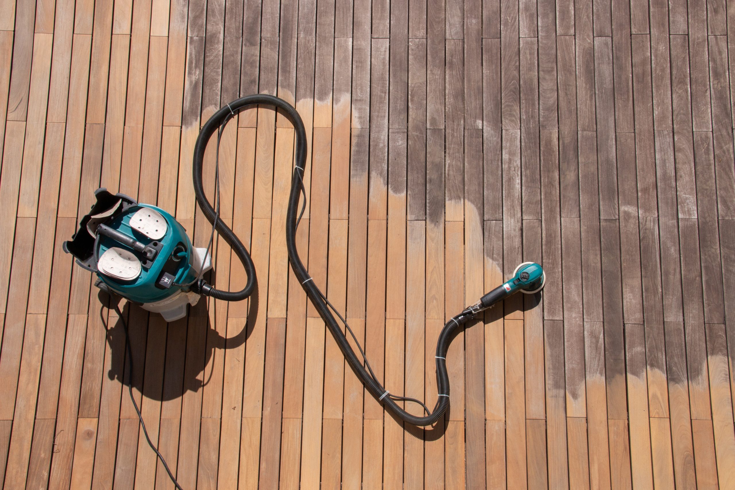 Wood Floor Sanding in Honor Oak on hardwood timber deck boards, showing a sanding machine restoring grey, weathered planks to fresh, clean wood.