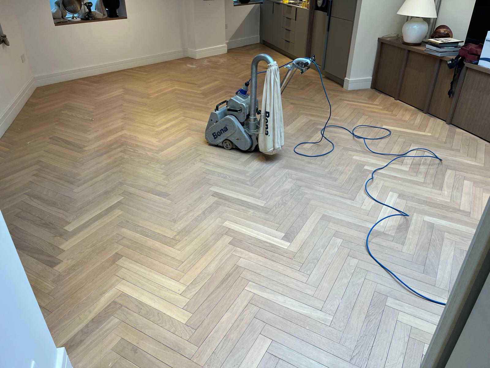 Wood Floor Sanding in Honor Oak on a light oak herringbone parquet floor, with a Bona sanding machine in the middle of the living room during restoration.Wood Floor Sanding in Honor Oak on a light oak herringbone parquet floor, with a Bona sanding machine in the middle of the living room during restoration.
