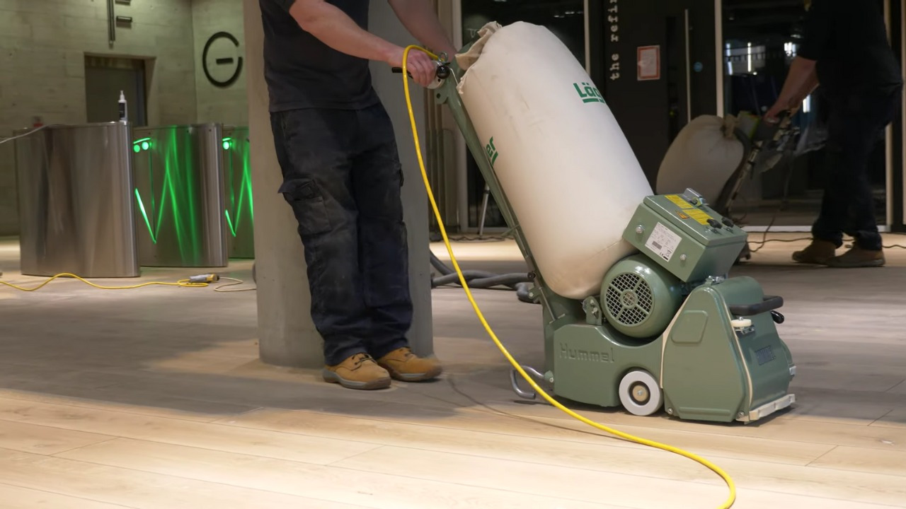 Commercial Floor Sanding in Honor Oak – light oak hardwood reception floor being sanded with a professional Lagler belt sander in a modern commercial entrance area.