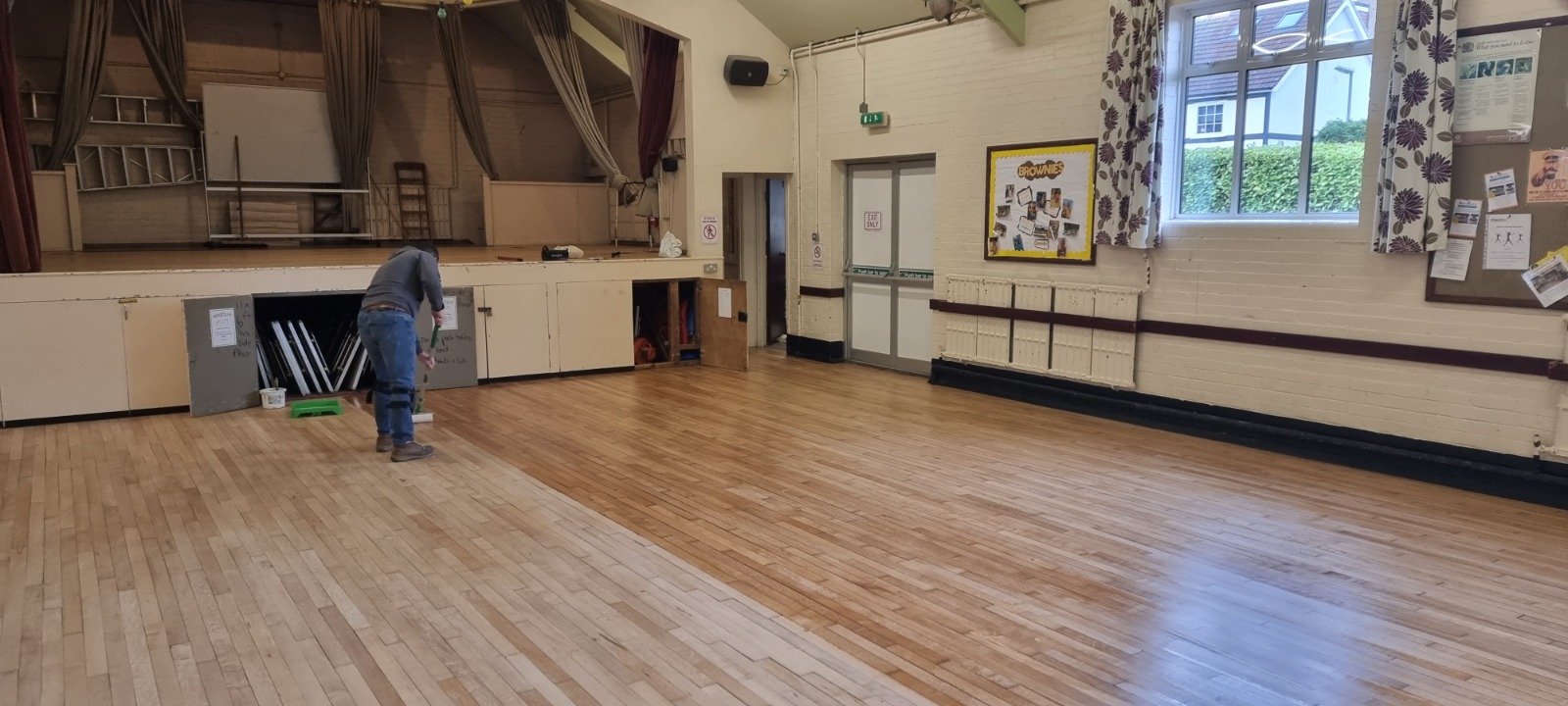 Commercial Floor Sanding in Honor Oak – technician applying finish to a maple strip hardwood community hall floor after sanding, revealing a warm, even sheen across the timber.