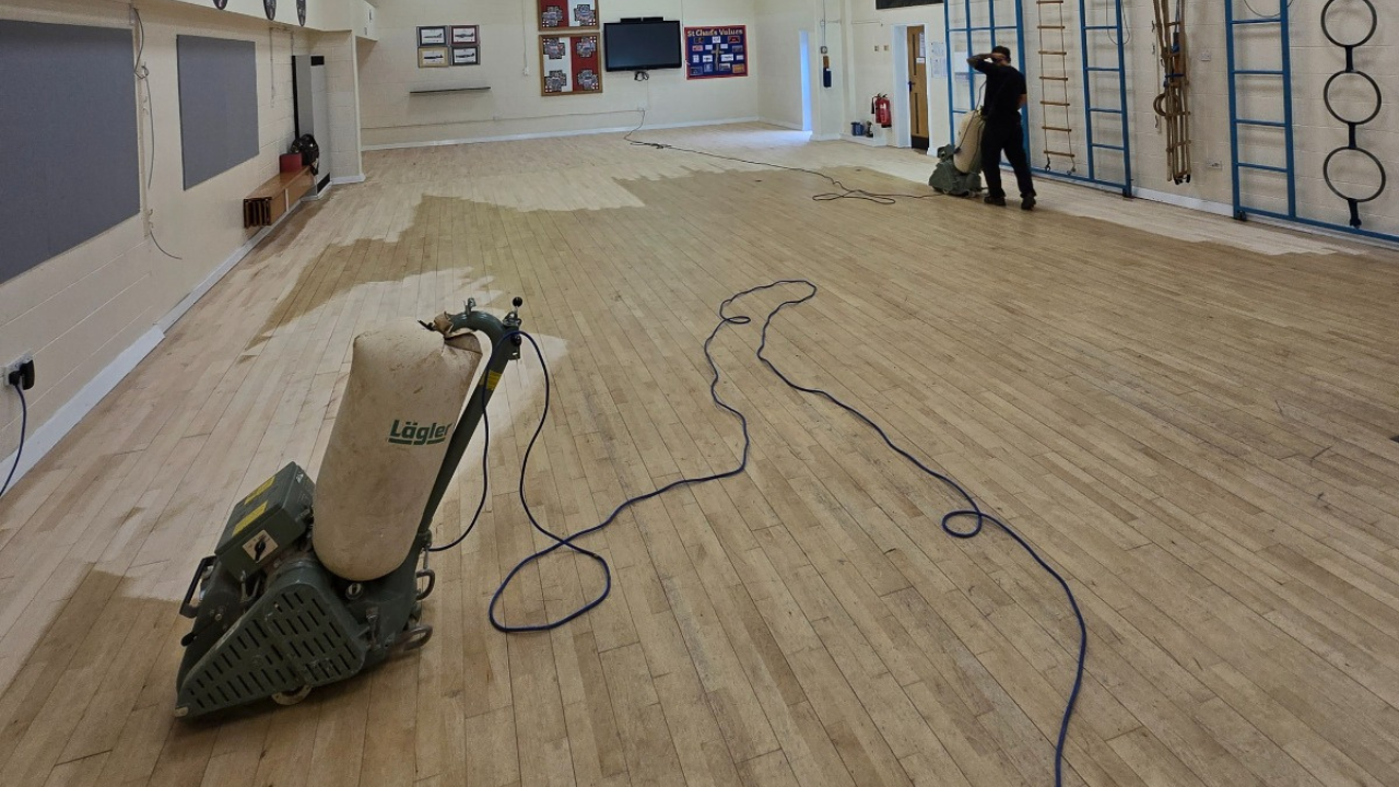 Commercial Floor Sanding in Honor Oak – maple strip hardwood school hall floor being sanded with professional machines, showing the transition from worn boards to freshly restored timber.