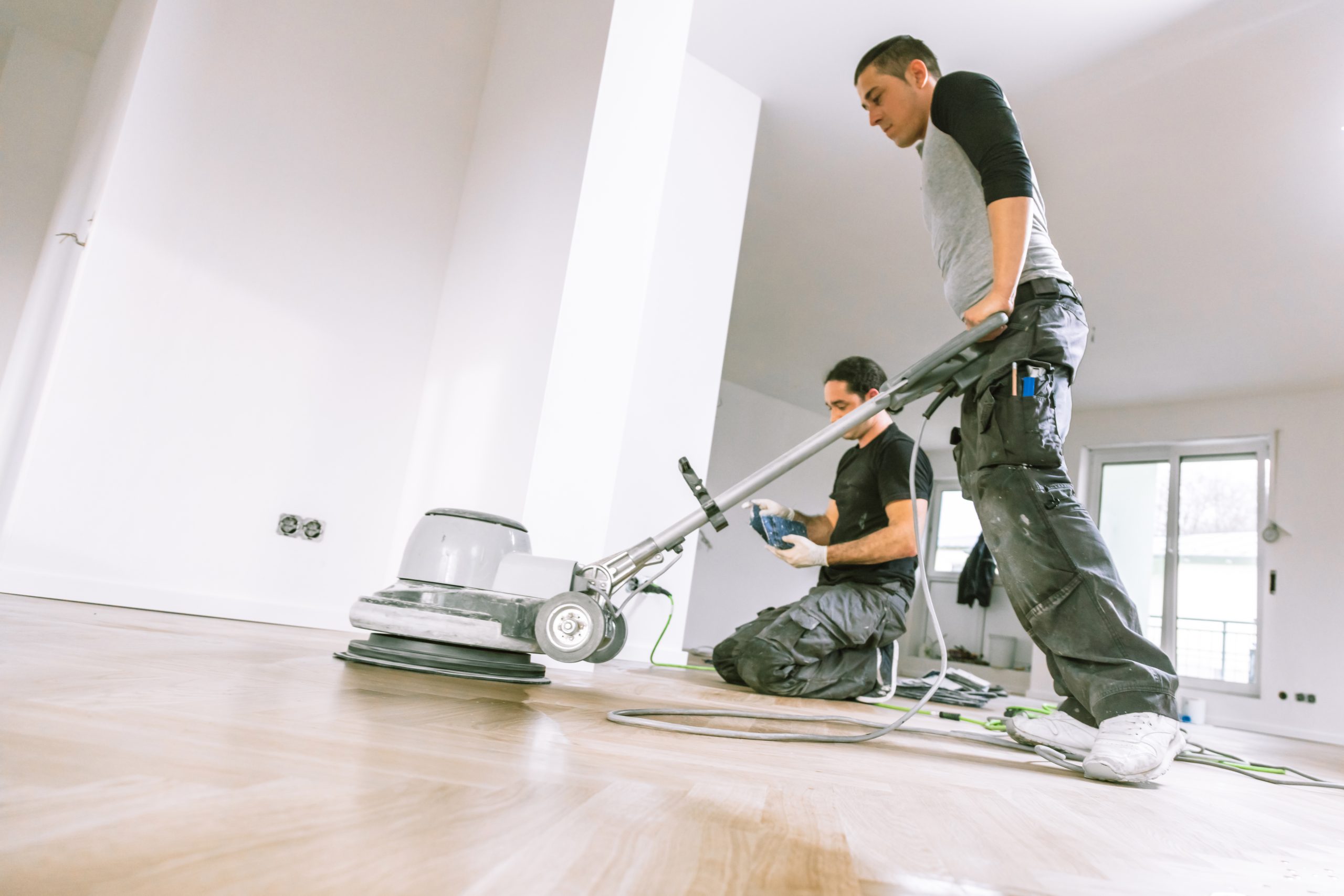 Commercial Floor Sanding in Honor Oak (honoroak) – two technicians sanding and refinishing an oak parquet wood floor in a bright commercial space.